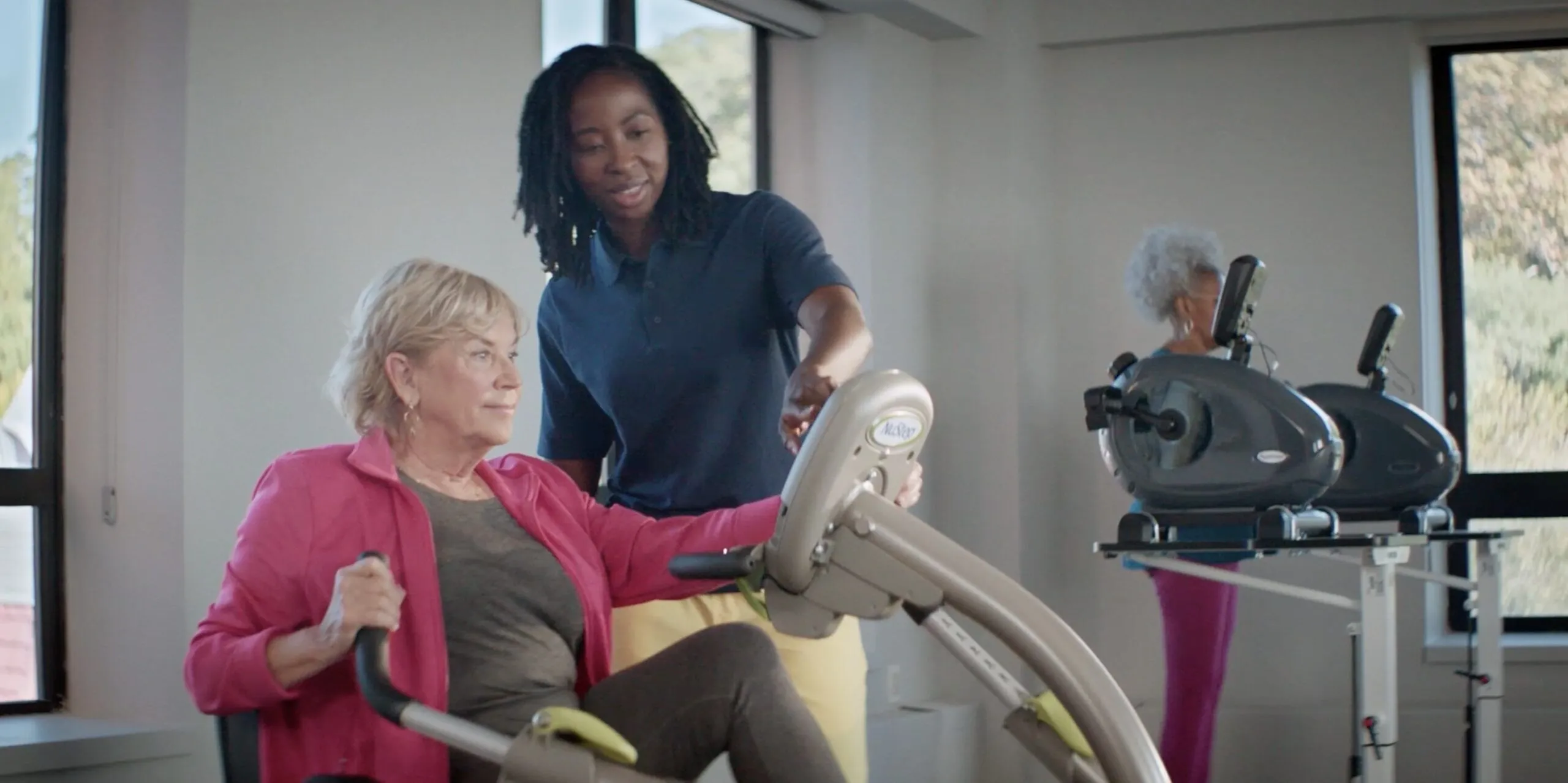 Older adult using rehabilitation equipment with support from a care professional