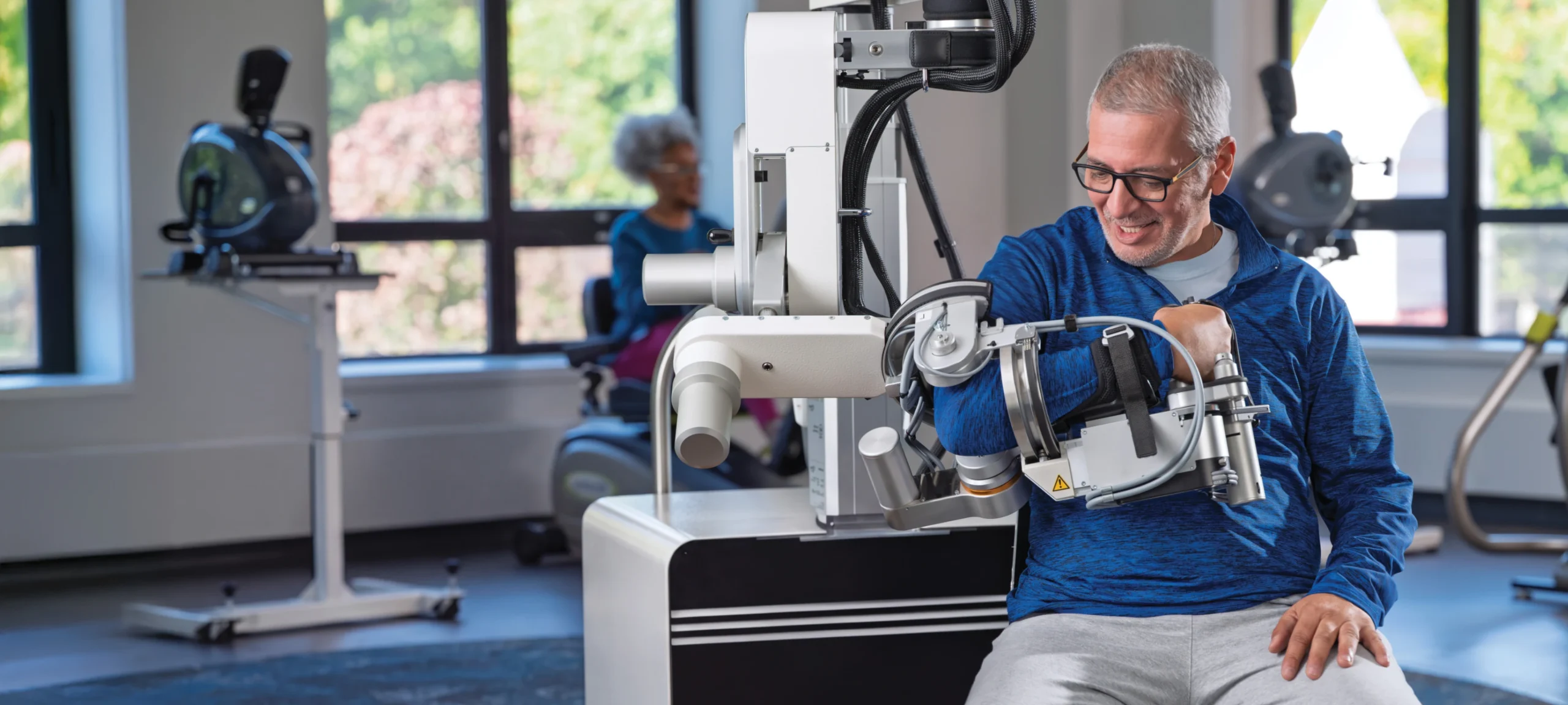 Man operates robotic arm rehab device in a well-lit, modern therapy clinic for short-term rehabilitation.