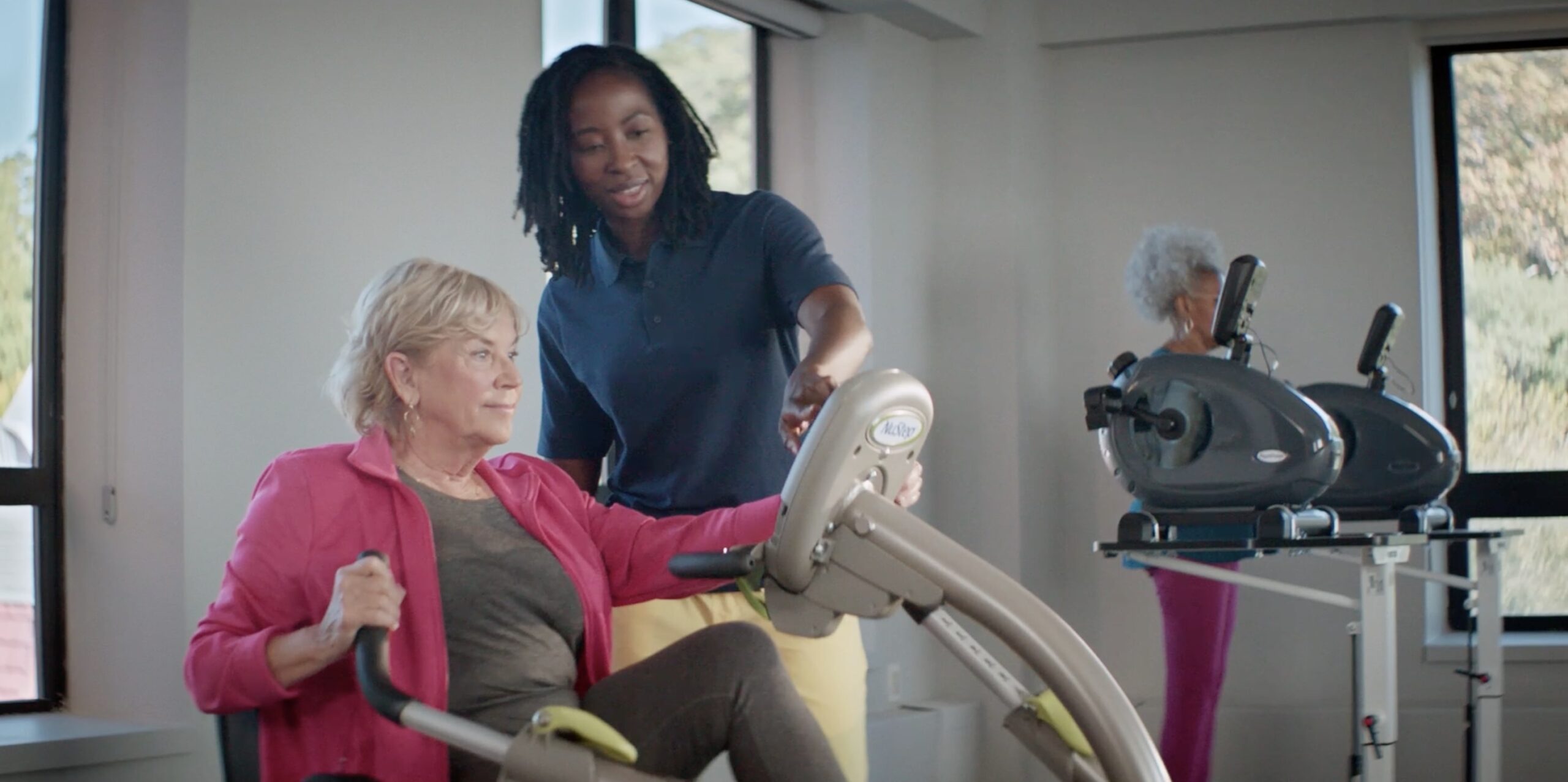 Older adult using rehabilitation equipment with support from a care professional
