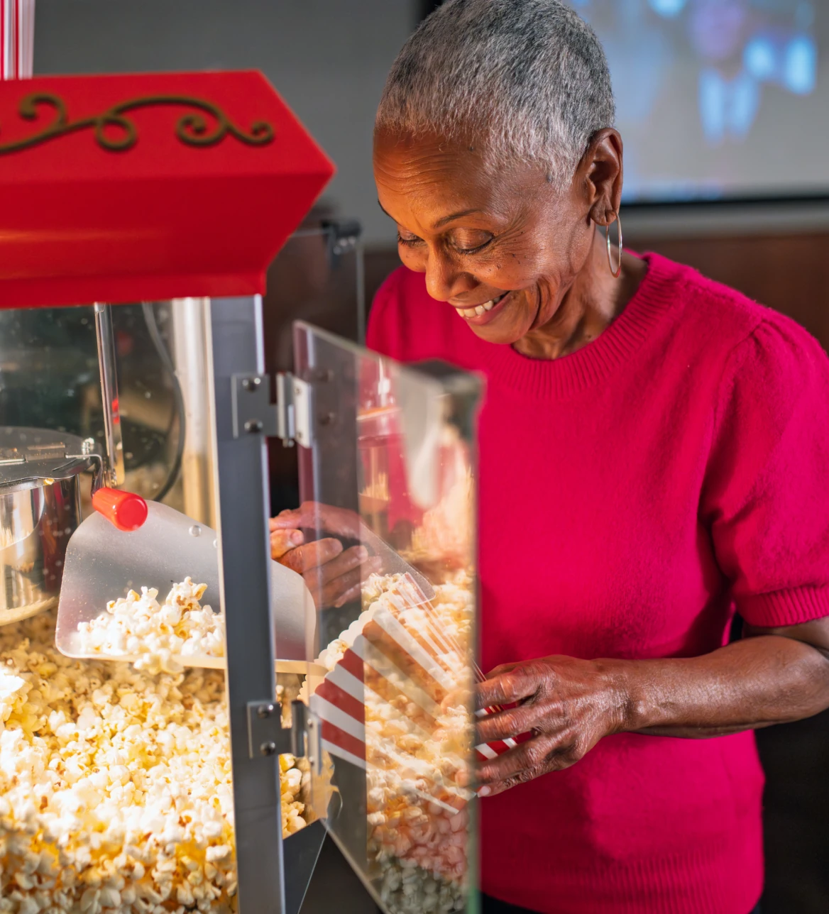 Smiling woman in red sweater scoops popcorn from a machine into a striped bag.