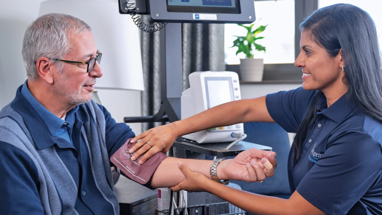 Healthcare worker checks a smiling man's blood pressure in a medical office at Hebrew Home.