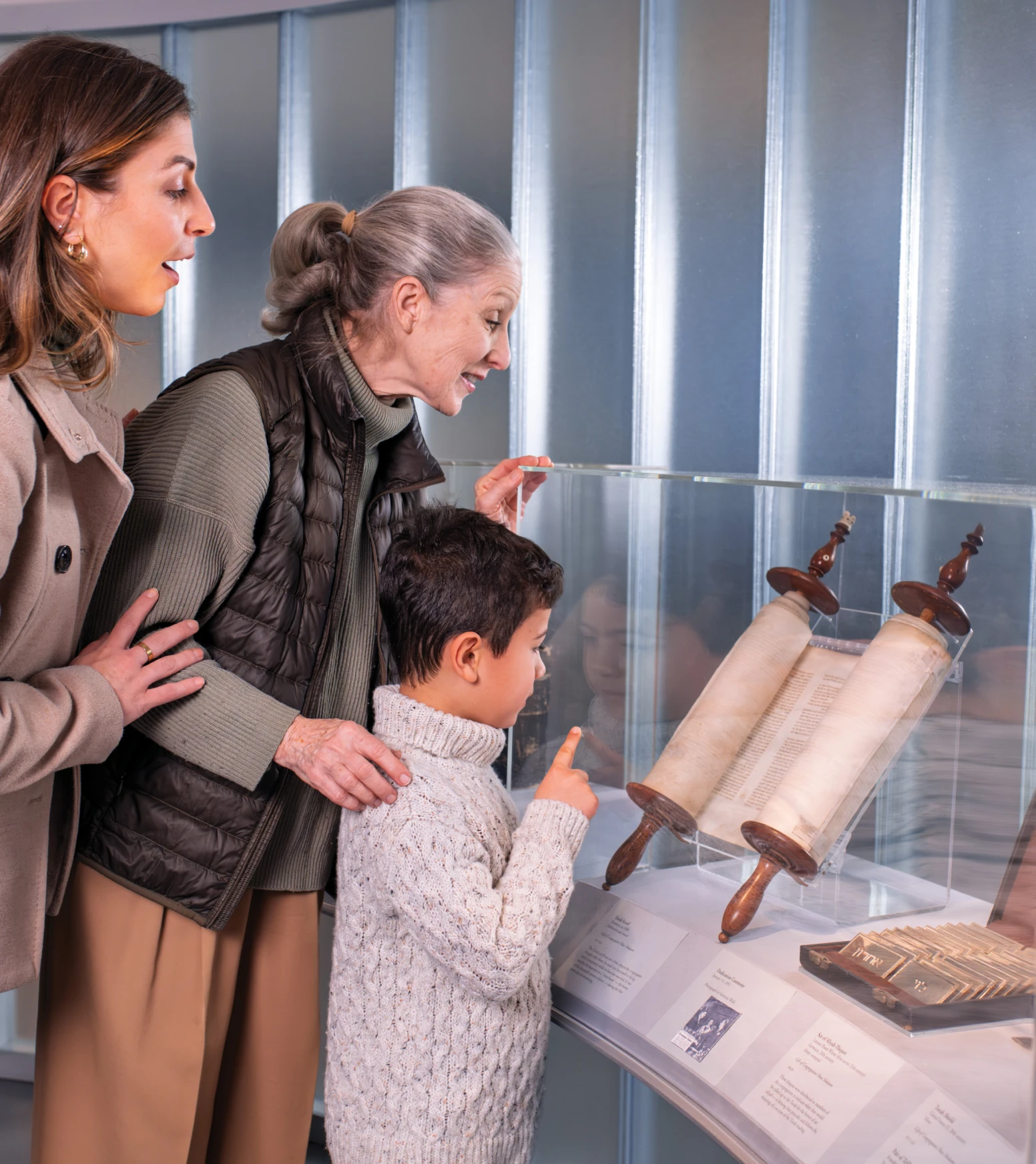 Three people view an ancient scroll in a glass case at a museum.