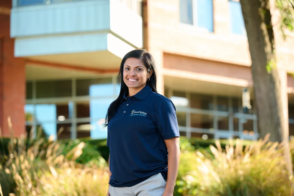 Smiling woman in navy polo stands outside a modern building with tall grass and large windows.