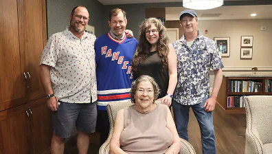 Five adults posing indoors, one older woman seated in front, four standing behind her.